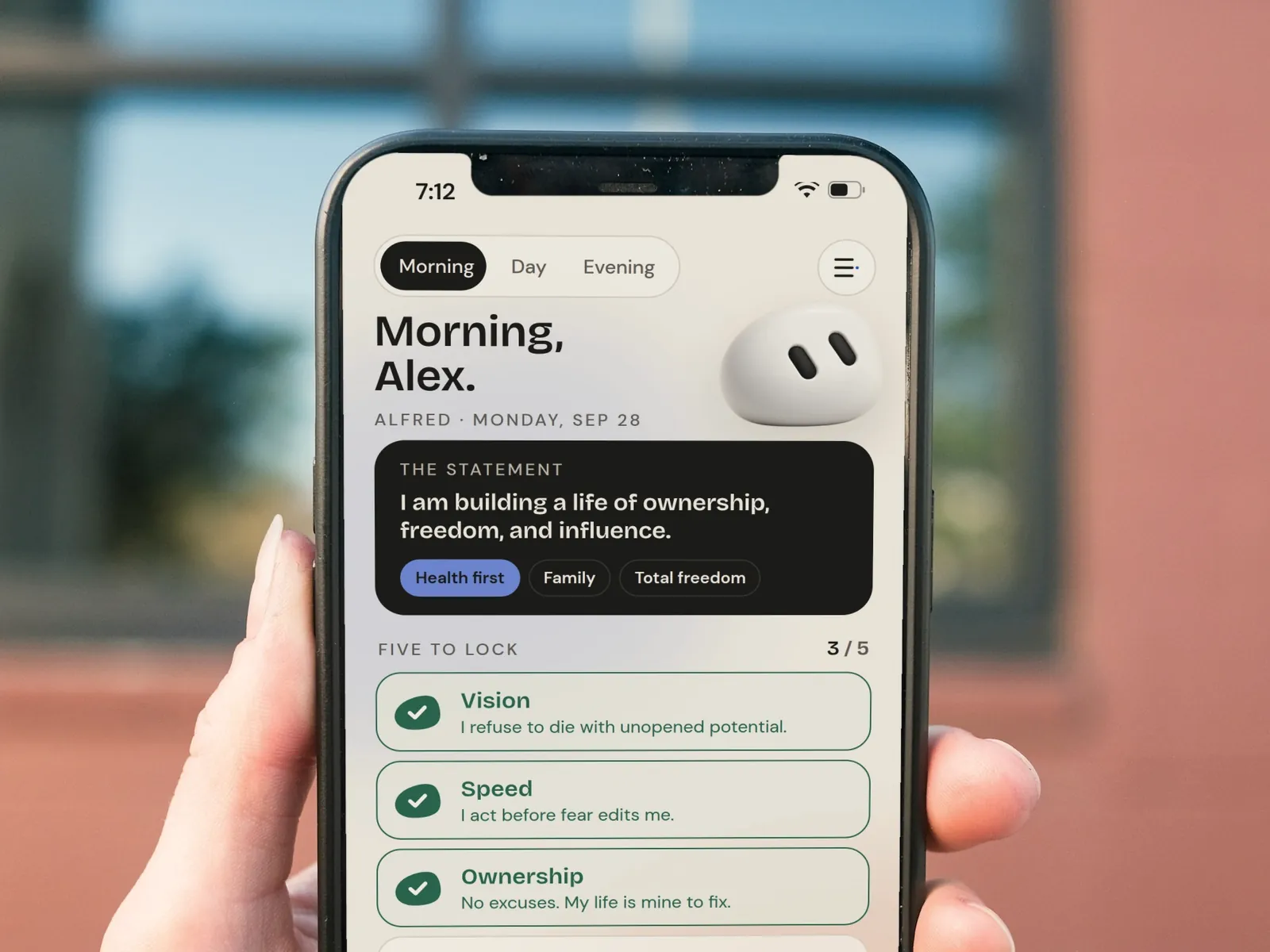 A hand holding an iPhone showing the Alfred morning screen